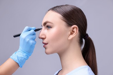 Photo of Doctor drawing marks on patient's nose for plastic surgery operation against grey background, closeup