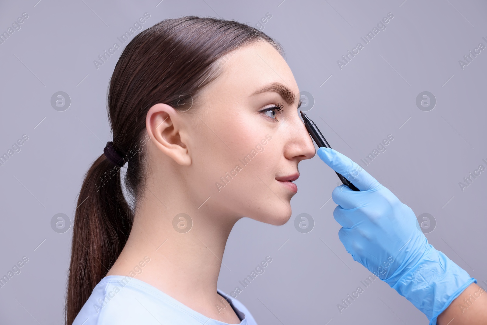 Photo of Doctor drawing marks on patient's nose for plastic surgery operation against grey background, closeup