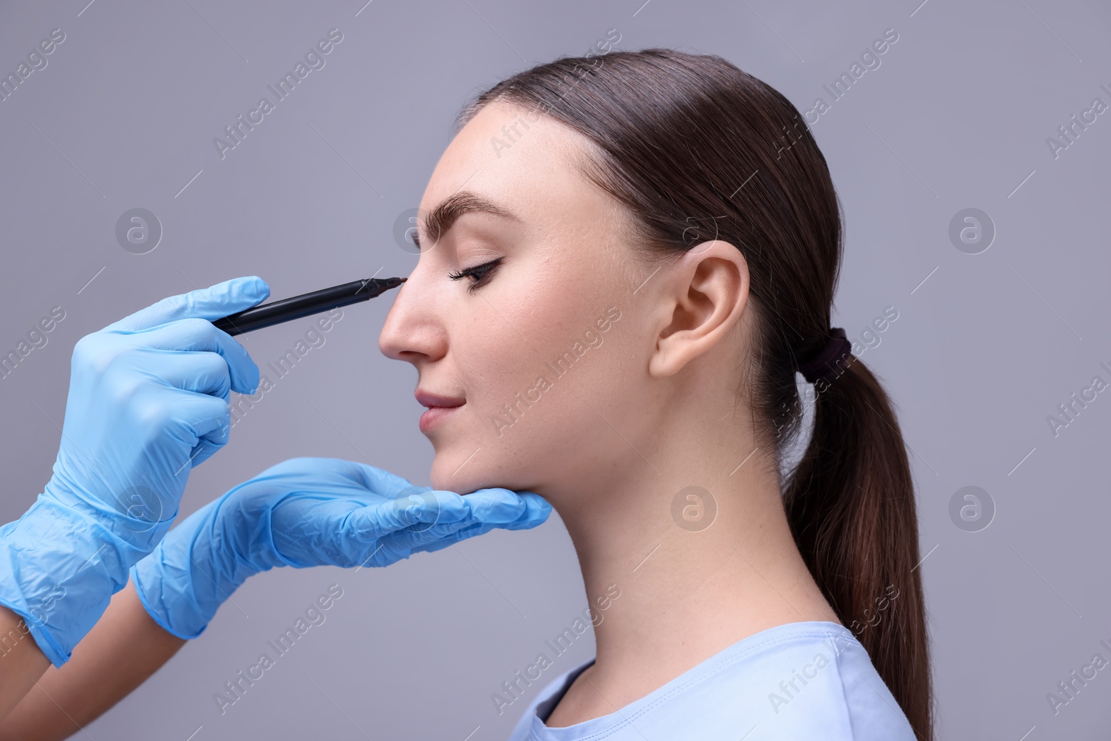 Photo of Doctor drawing marks on patient's nose for plastic surgery operation against grey background, closeup