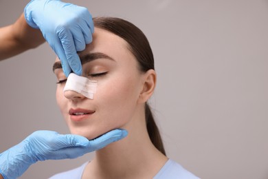 Photo of Doctor checking patient's nose after plastic surgery operation on grey background, closeup. Space for text