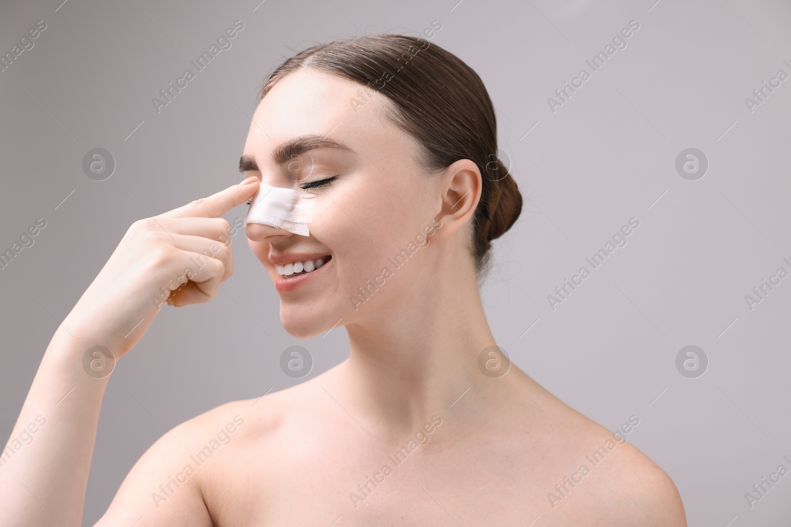 Photo of Woman with medical bandage on her nose after plastic surgery operation against grey background