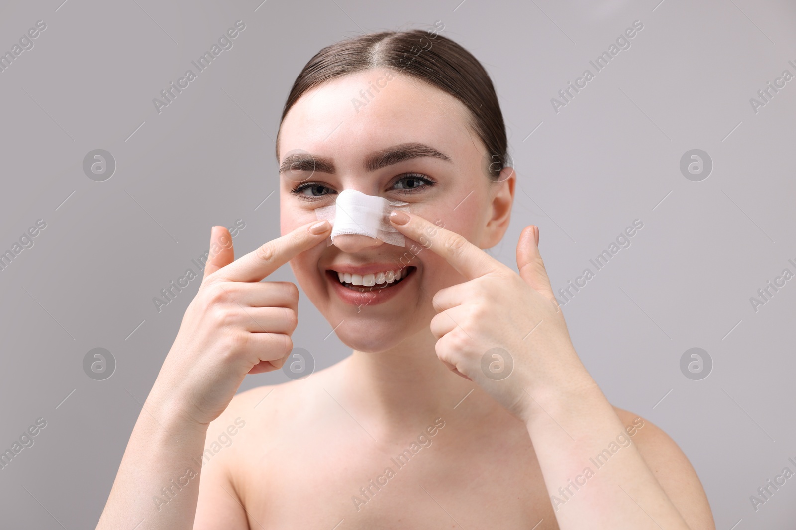 Photo of Woman with medical bandage on her nose after plastic surgery operation against grey background