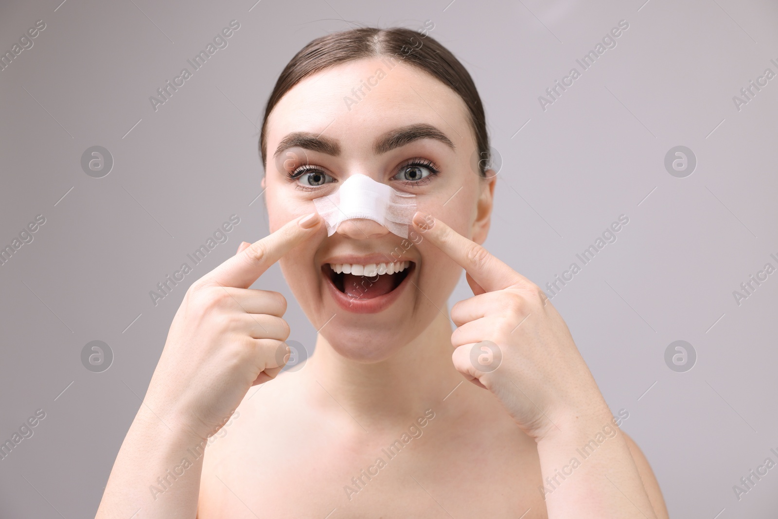 Photo of Woman with medical bandage on her nose after plastic surgery operation against grey background