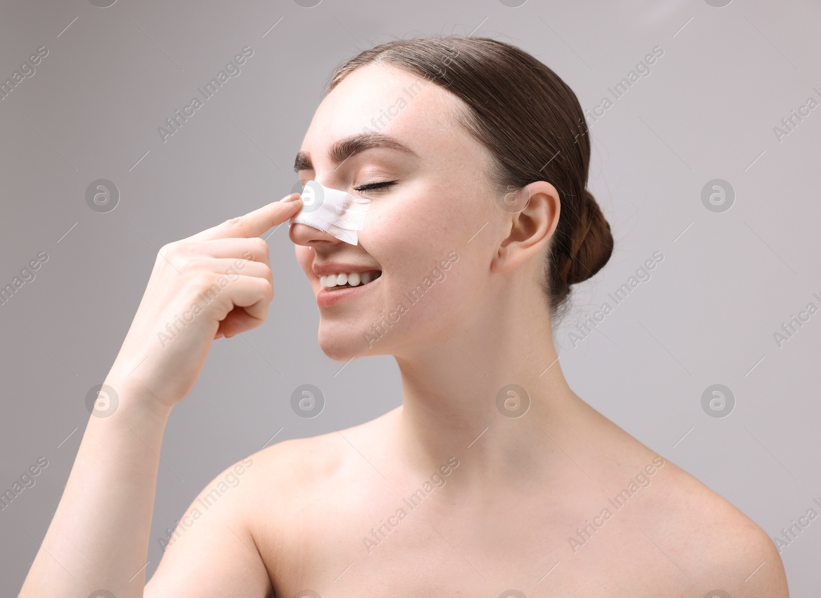 Photo of Woman with medical bandage on her nose after plastic surgery operation against grey background