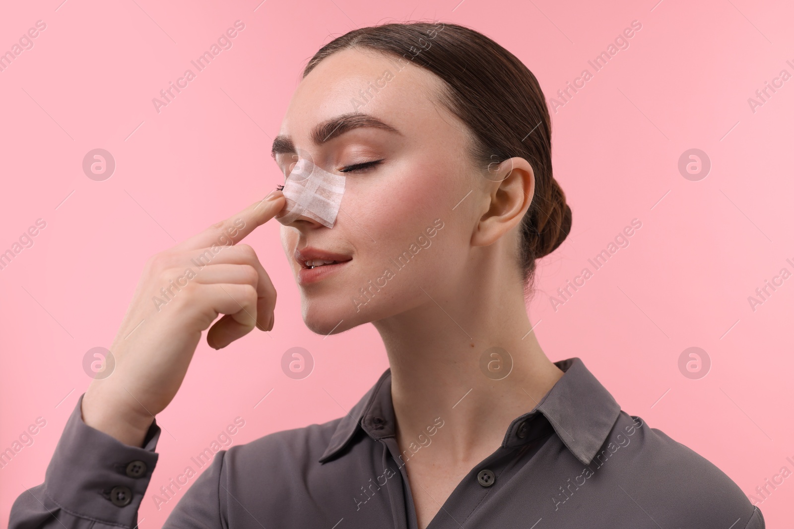 Photo of Woman with medical bandage on her nose after plastic surgery operation against pink background