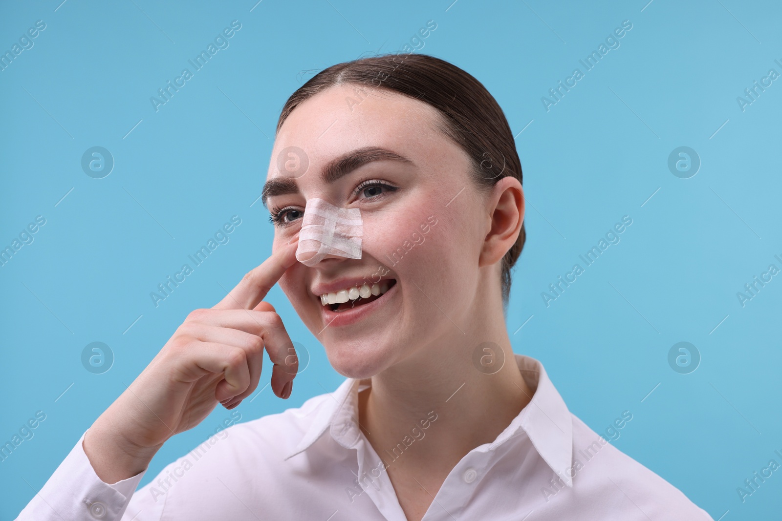 Photo of Woman with medical bandage on her nose after plastic surgery operation against light blue background