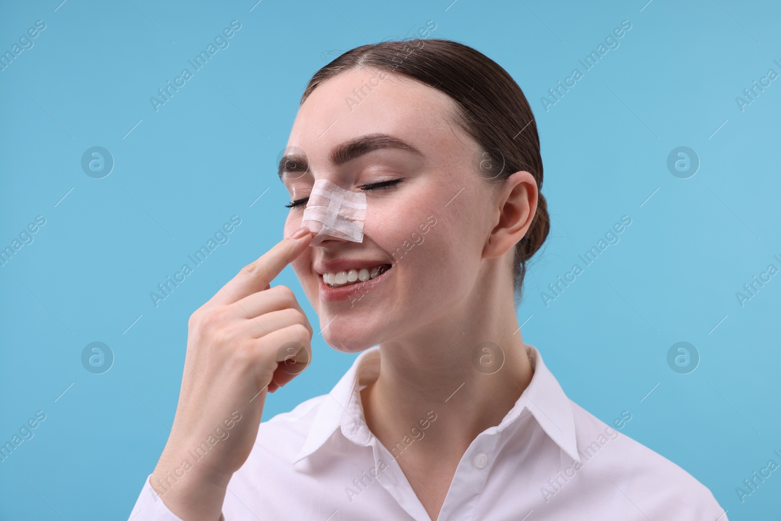 Photo of Woman with medical bandage on her nose after plastic surgery operation against light blue background