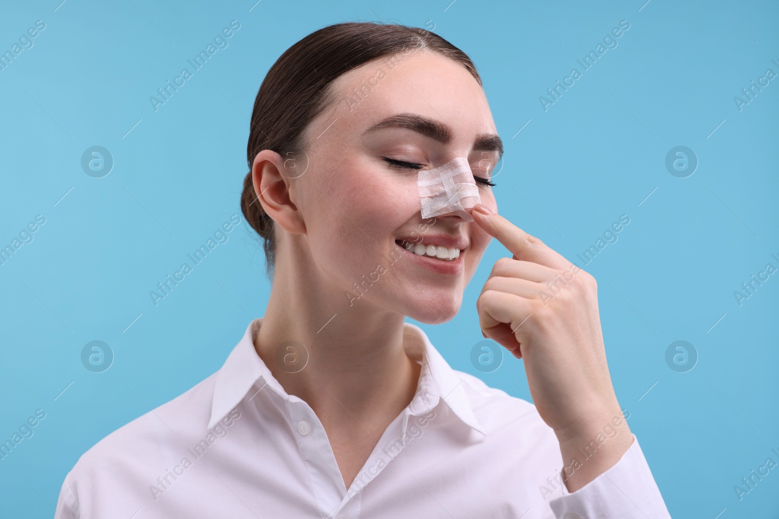 Photo of Woman with medical bandage on her nose after plastic surgery operation against light blue background