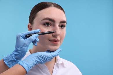 Photo of Doctor drawing marks on patient's nose for plastic surgery operation against light blue background, , closeup. Space for text