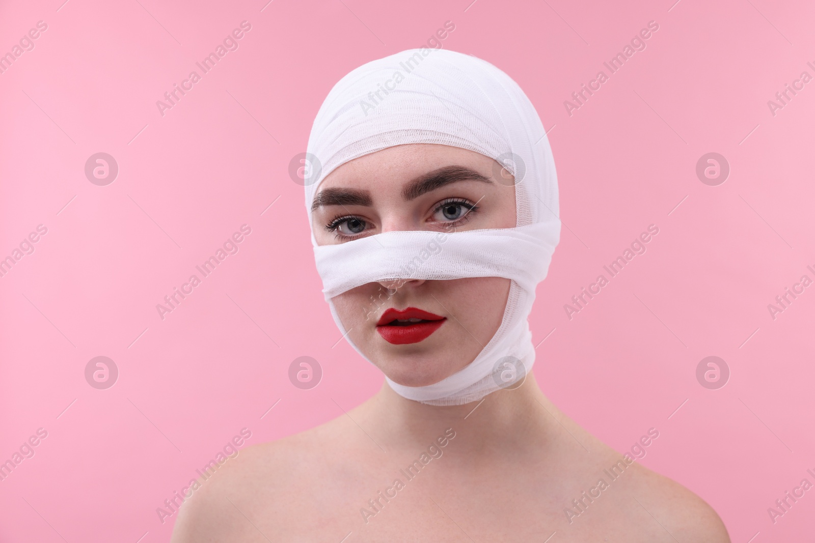 Photo of Woman with nose wrapped in medical bandage after plastic surgery operation on pink background