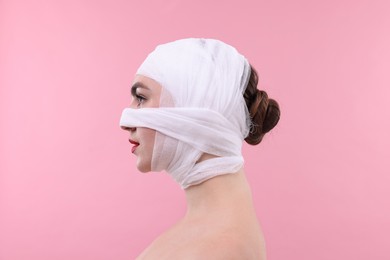 Photo of Woman with nose wrapped in medical bandage after plastic surgery operation on pink background