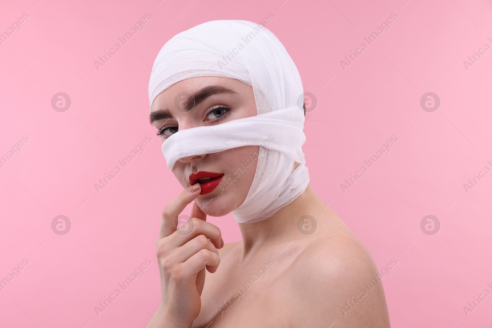 Photo of Woman with nose wrapped in medical bandage after plastic surgery operation on pink background