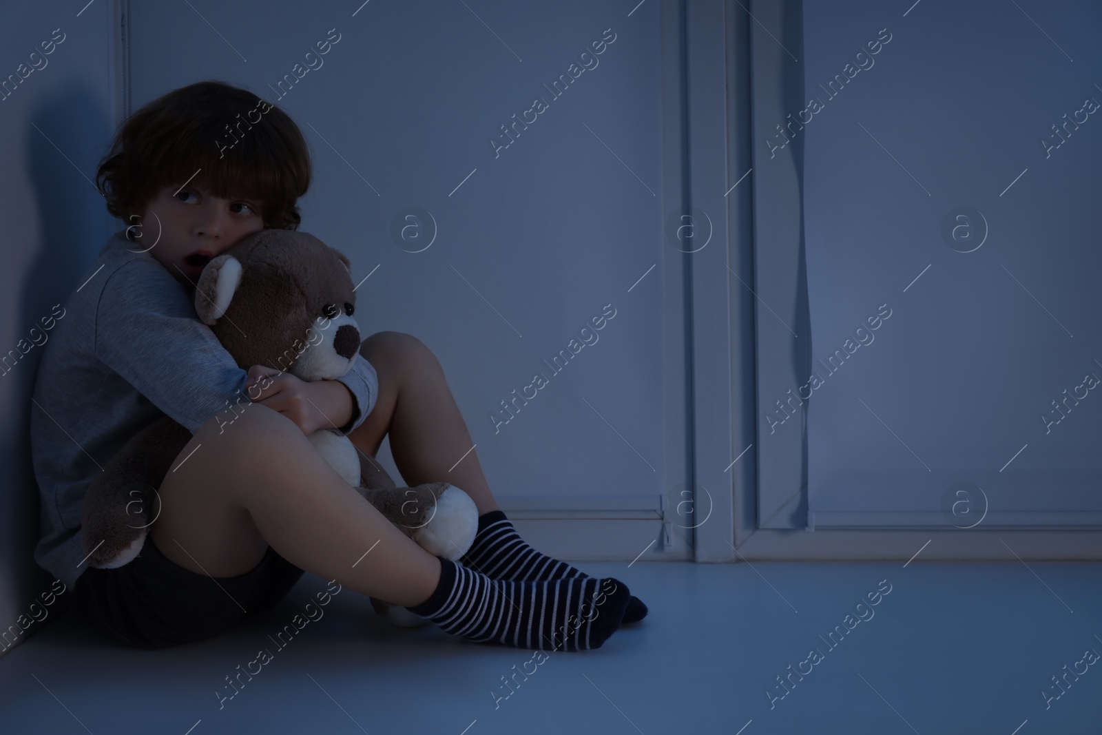 Photo of Fearful boy hiding with teddy bear on windowsill at night. Space for text