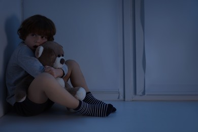 Photo of Fearful boy hiding with teddy bear on windowsill at night. Space for text