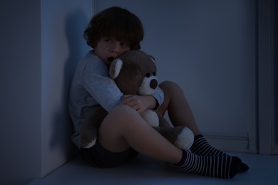 Photo of Fearful boy hiding with teddy bear on windowsill at night