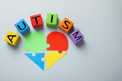 Photo of Colorful cubes with word Autism and heart made of puzzle pieces on grey background, flat lay. Space for text