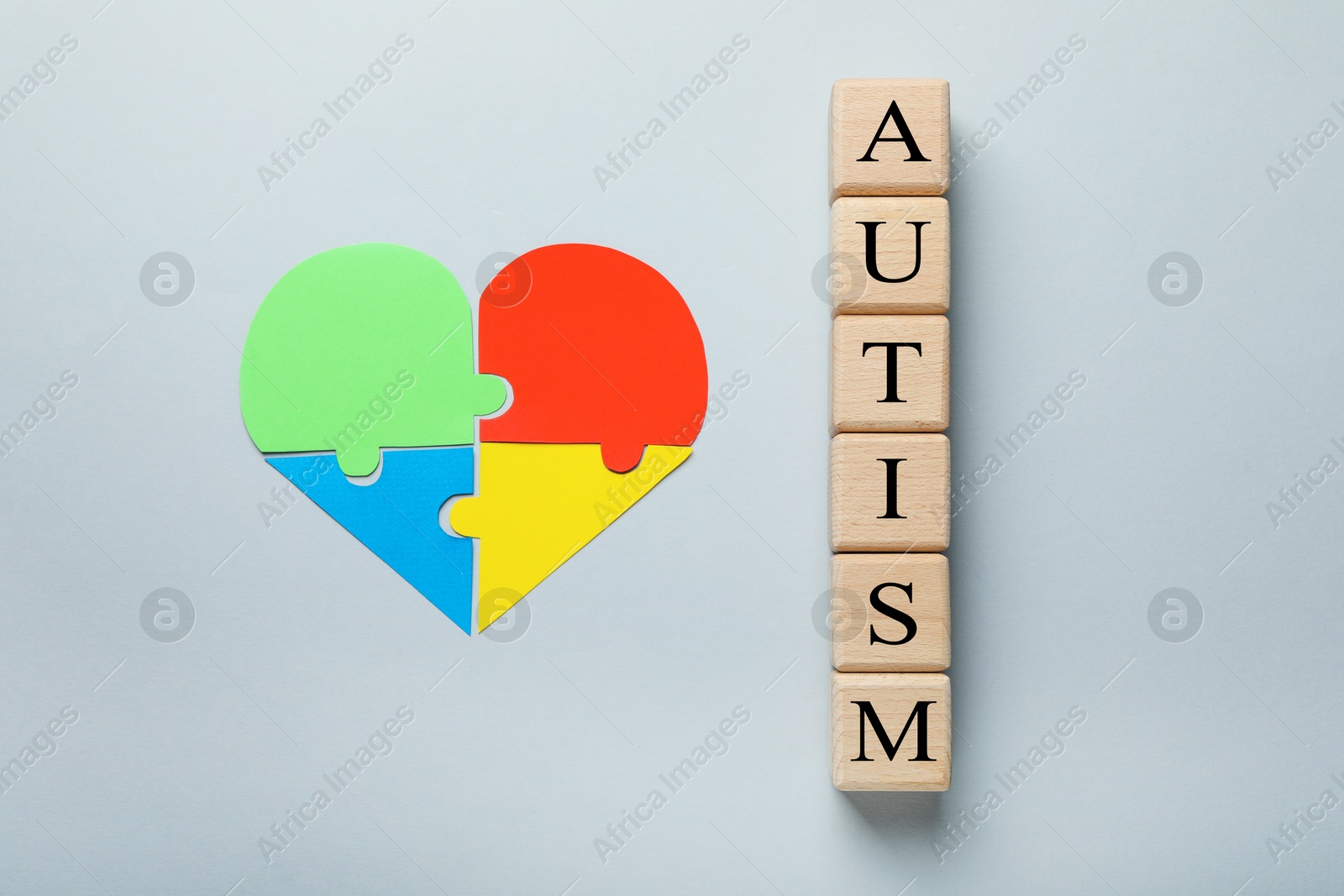 Photo of Wooden cubes with word Autism and heart made of puzzle pieces on grey background, flat lay