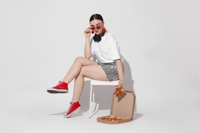 Photo of Woman in sunglasses with delicious pizza sitting on chair against white background