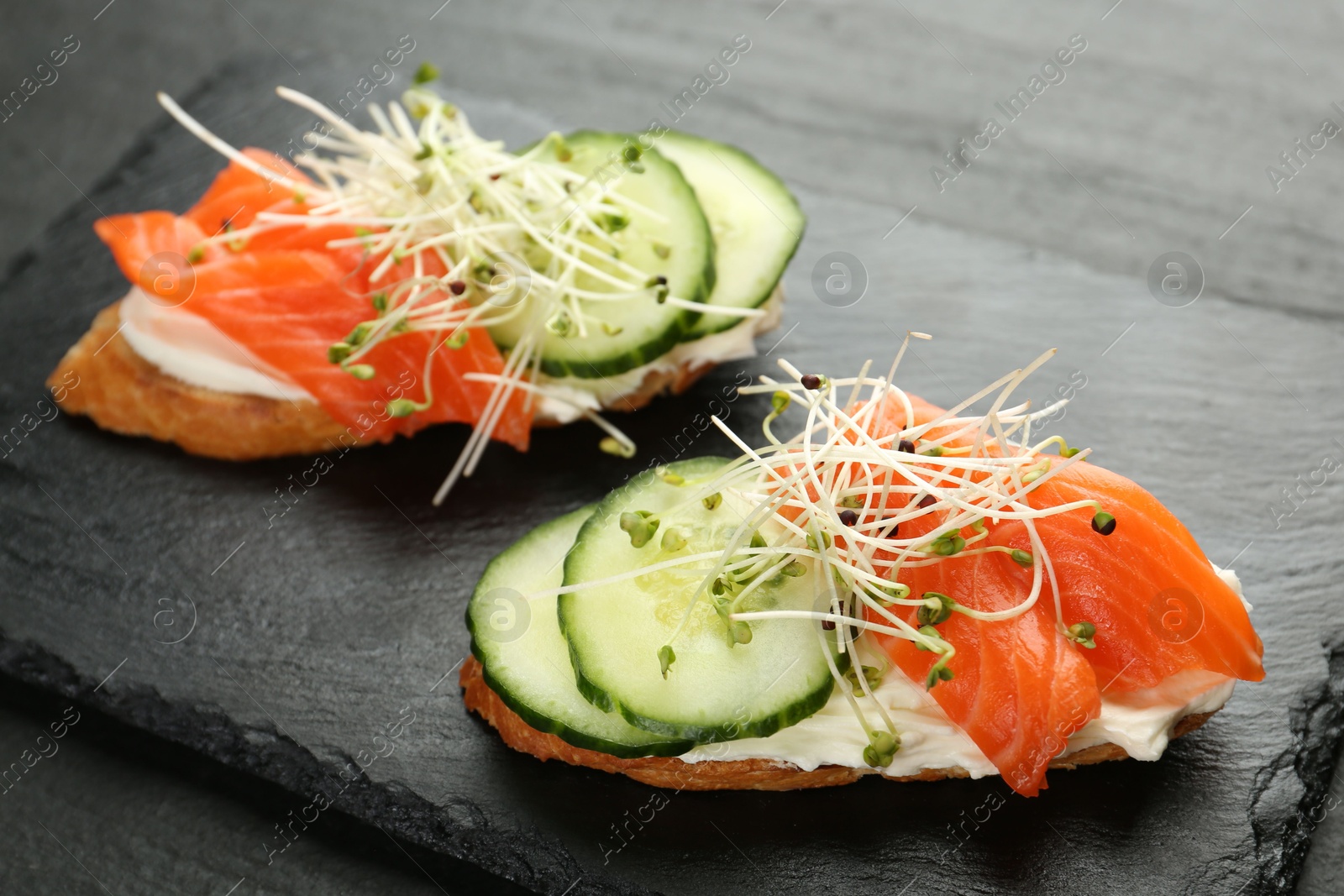 Photo of Delicious bruschette with salmon, cream cheese and cucumber on grey table, closeup