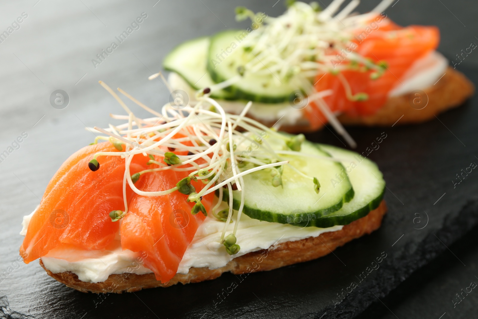 Photo of Delicious bruschette with salmon, cream cheese and cucumber on grey table, closeup