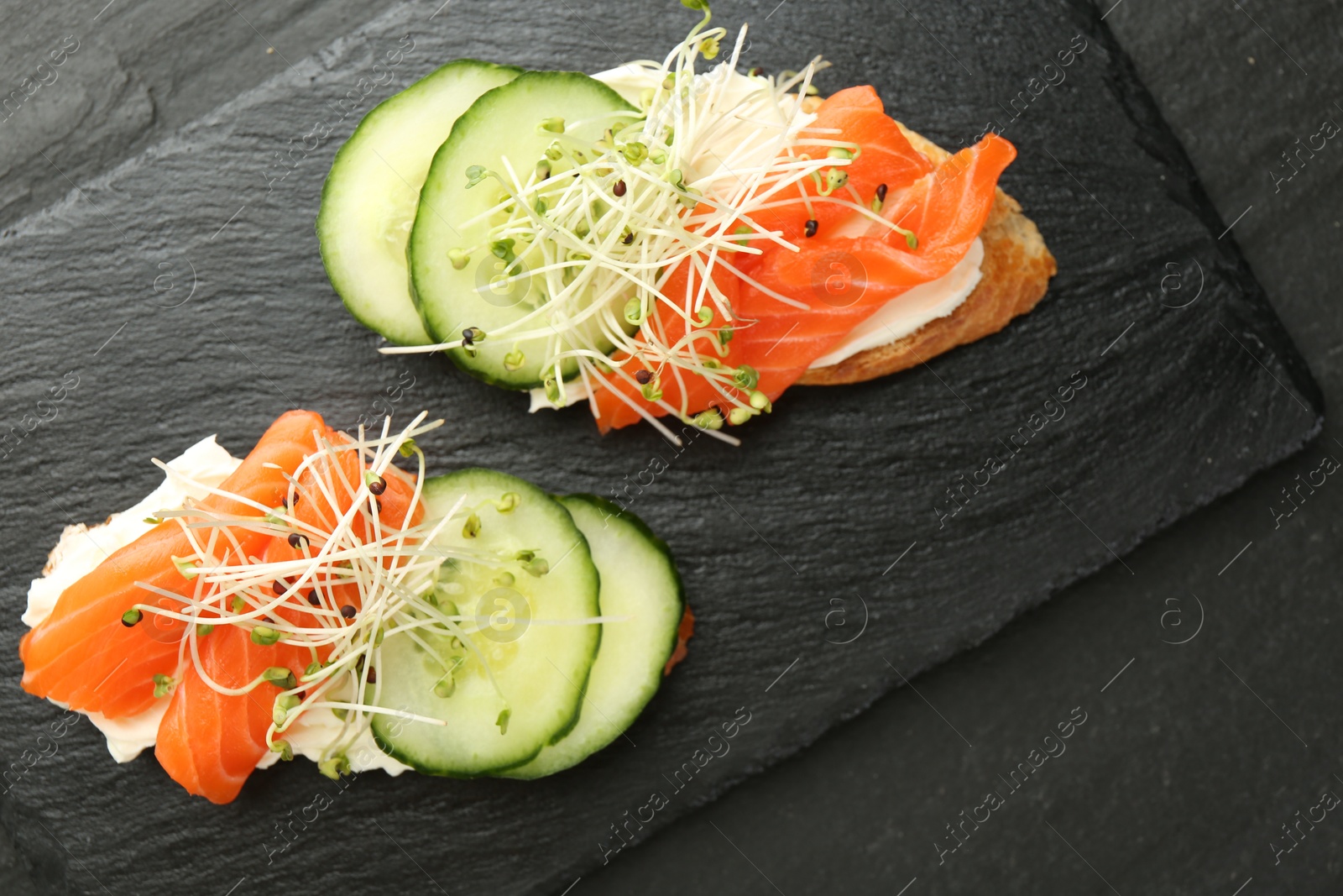 Photo of Delicious bruschette with salmon, cream cheese and cucumber on grey table, top view