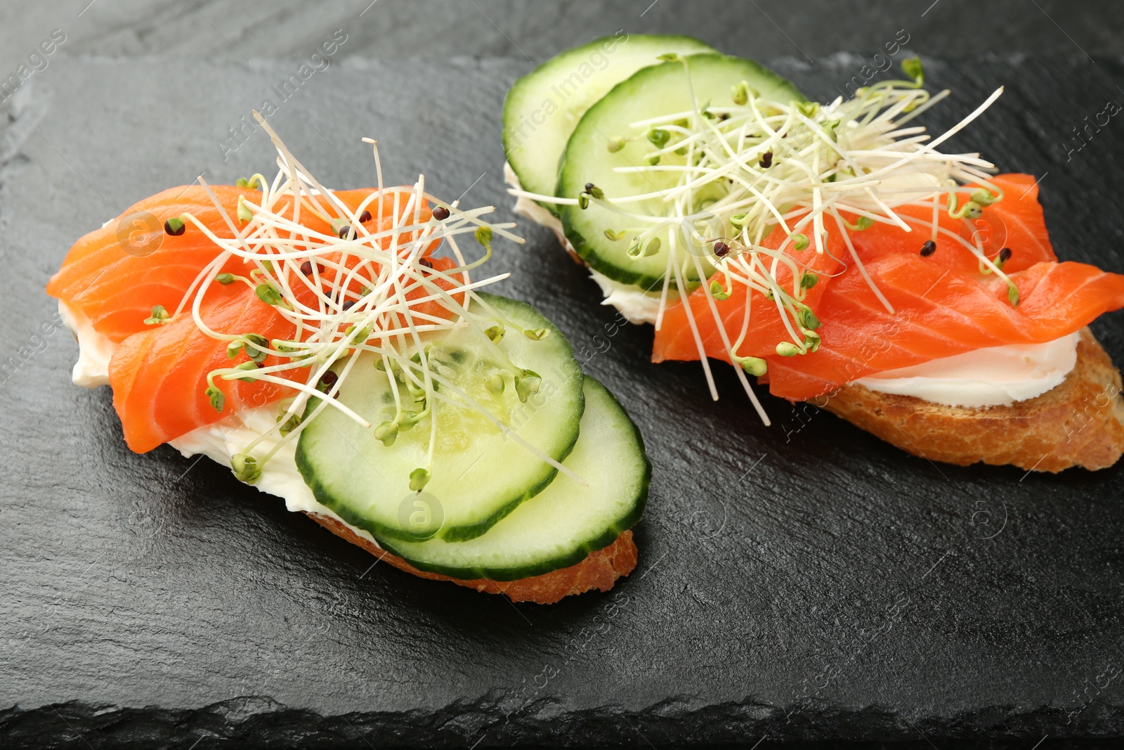 Photo of Delicious bruschette with salmon, cream cheese and cucumber on grey table, closeup