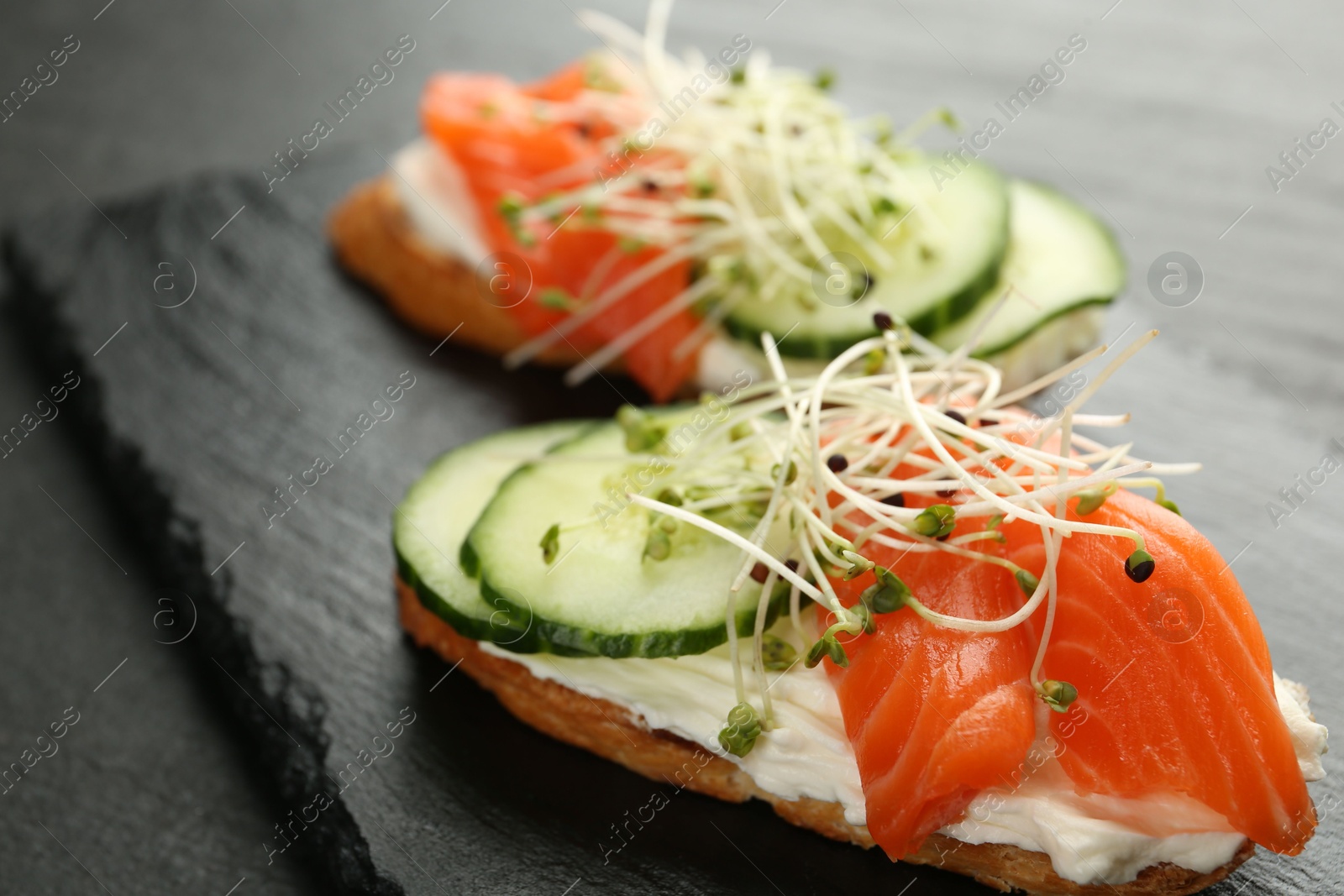 Photo of Delicious bruschette with salmon, cream cheese and cucumber on grey table, closeup