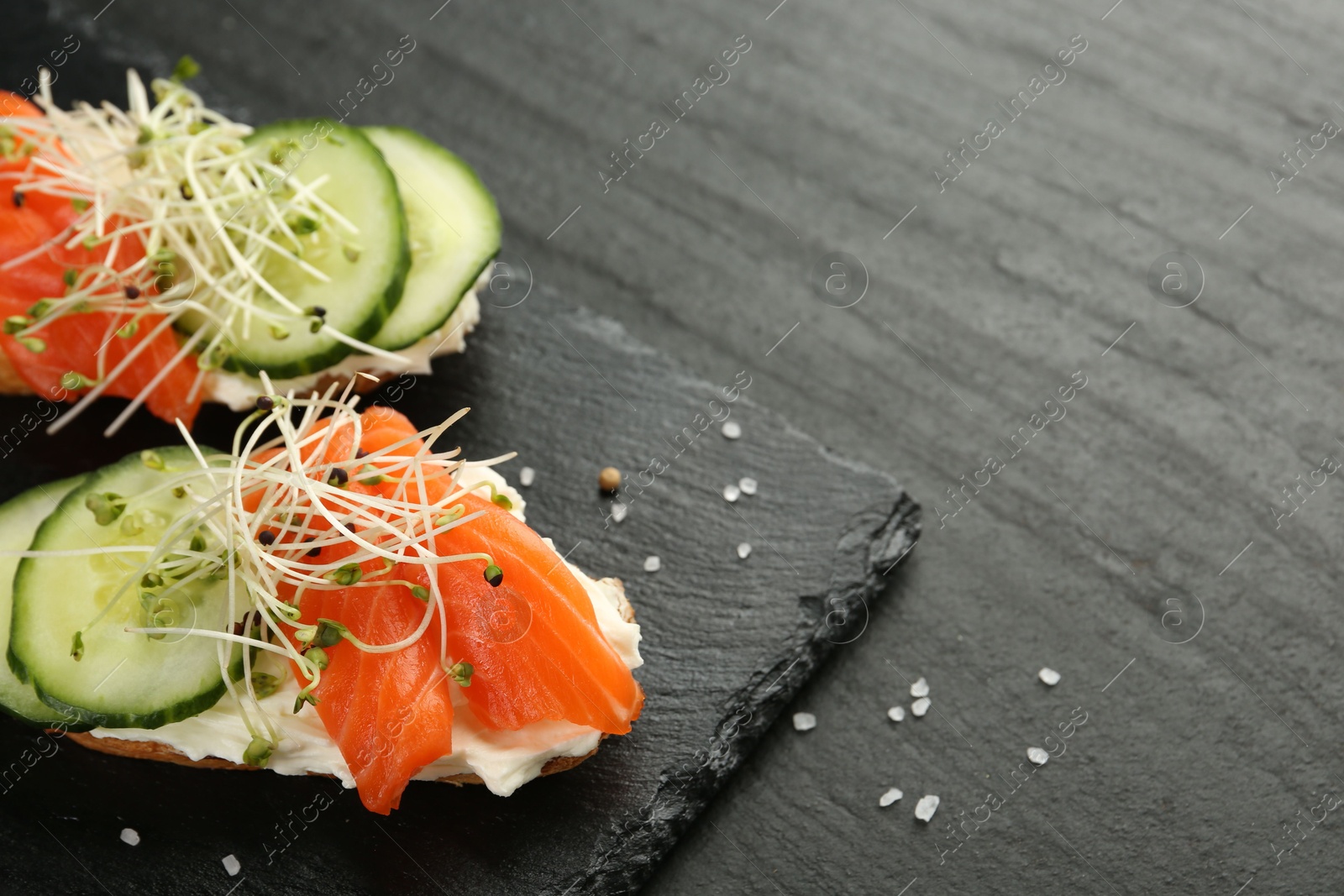 Photo of Delicious bruschette with salmon, cream cheese and cucumber on grey table, closeup. Space for text