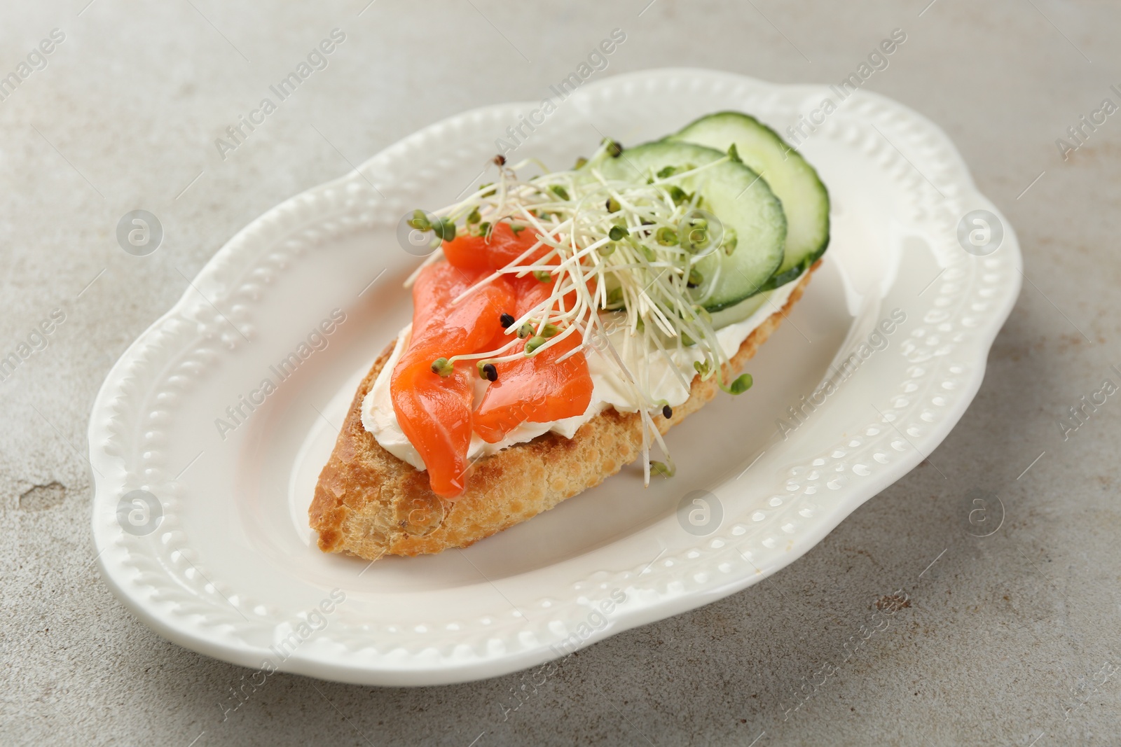 Photo of Delicious bruschetta with salmon, cream cheese and cucumber on light table, closeup