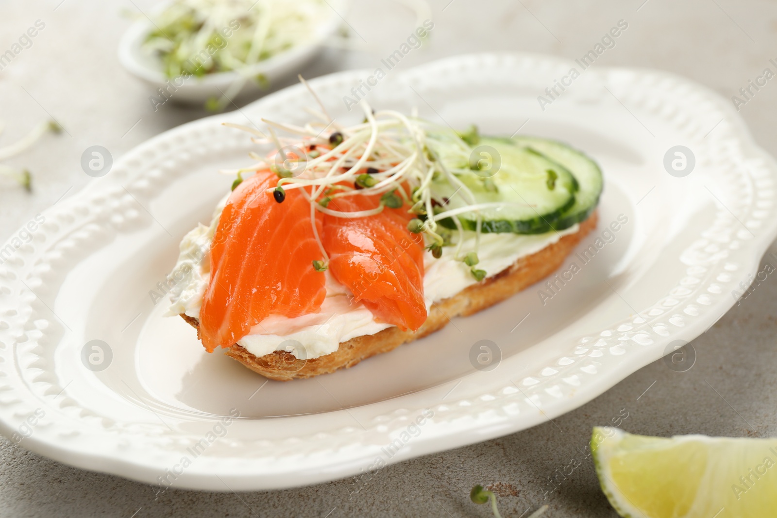 Photo of Delicious bruschetta with salmon, cream cheese and cucumber on light table, closeup