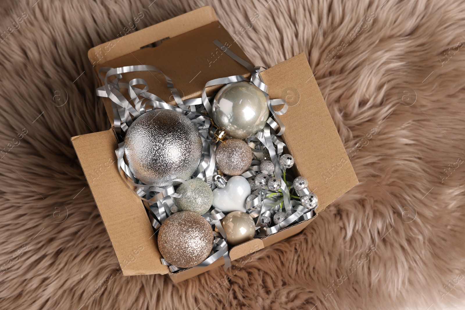 Photo of Shiny tinsel and other Christmas decor in cardboard box on rug, top view