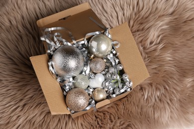 Photo of Shiny tinsel and other Christmas decor in cardboard box on rug, top view