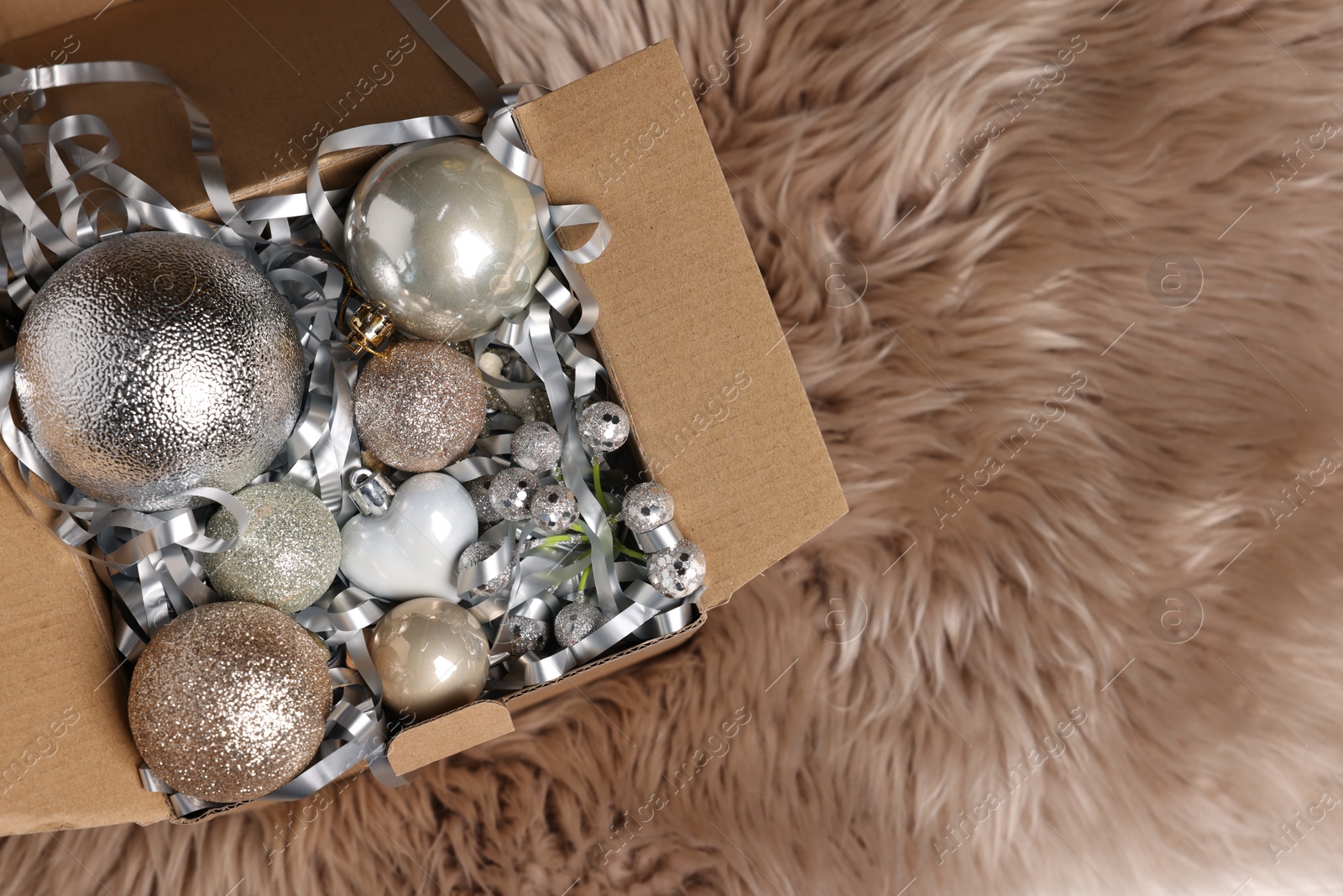 Photo of Shiny tinsel and other Christmas decor in cardboard box on rug, top view. Space for text