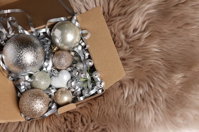 Photo of Shiny tinsel and other Christmas decor in cardboard box on rug, top view. Space for text