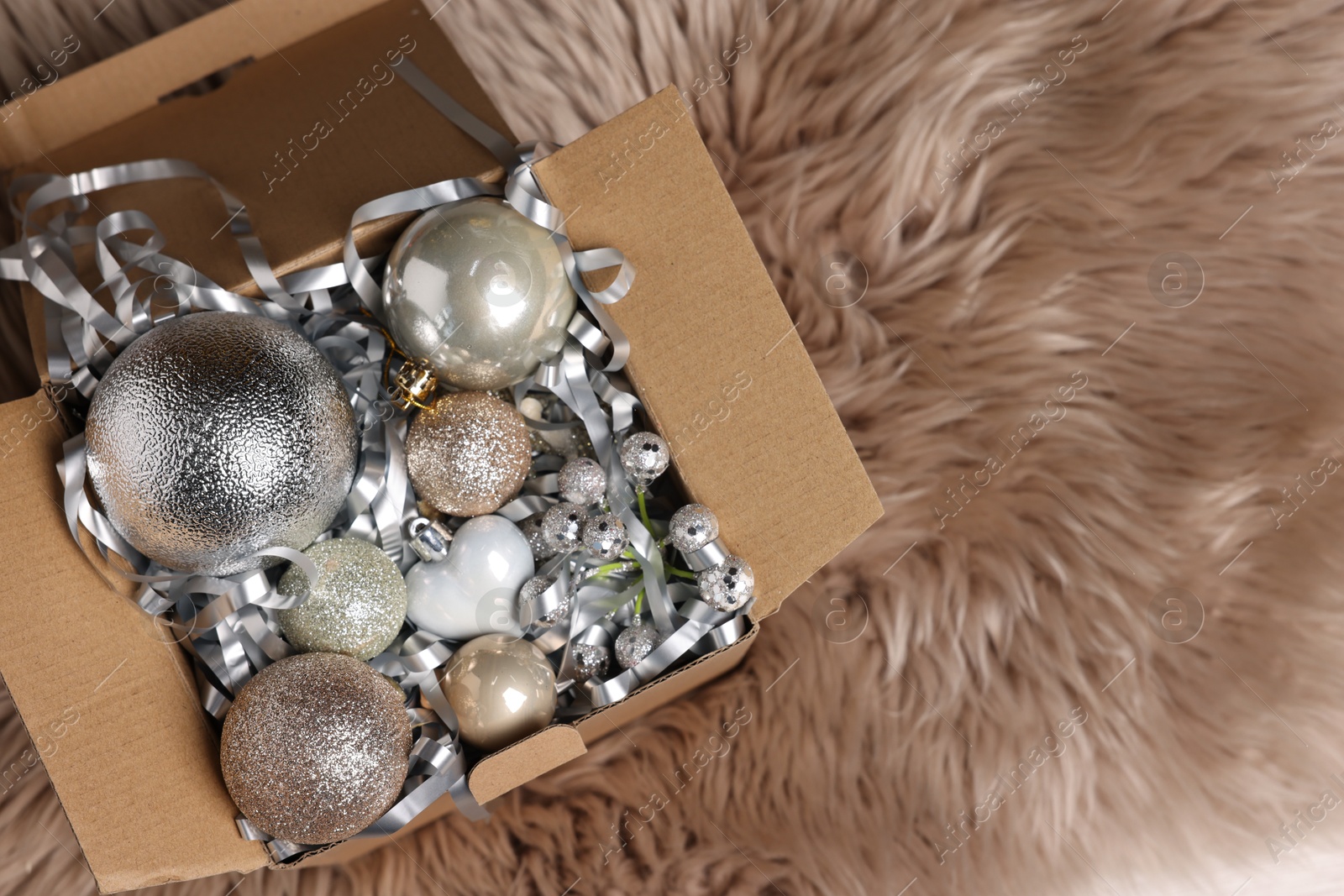 Photo of Shiny tinsel and other Christmas decor in cardboard box on rug, top view. Space for text