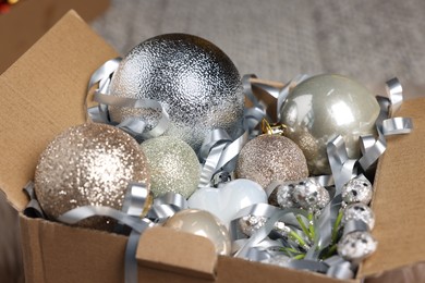 Photo of Shiny tinsel and Christmas balls in cardboard box indoors, closeup