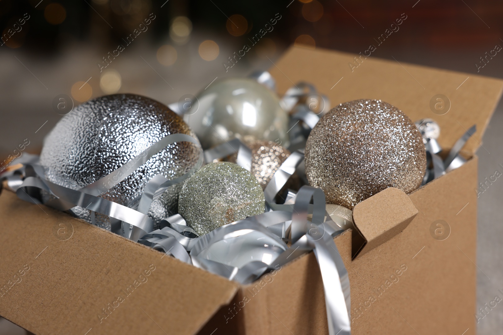 Photo of Shiny tinsel and Christmas balls in cardboard box indoors, closeup