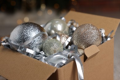 Photo of Shiny tinsel and Christmas balls in cardboard box indoors, closeup