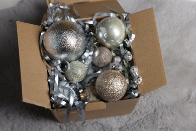 Photo of Shiny tinsel and Christmas balls in cardboard box on carpet