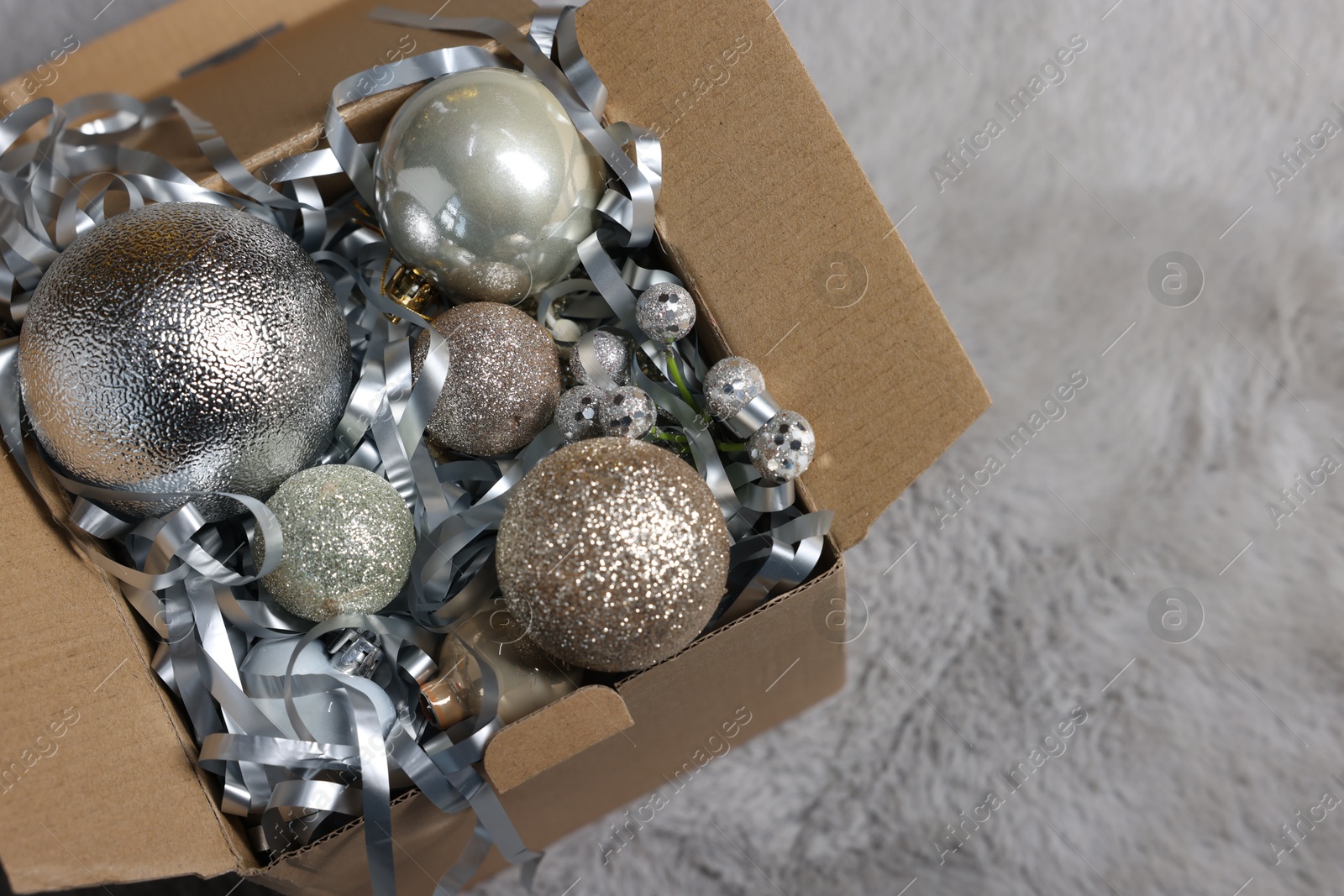 Photo of Shiny tinsel and Christmas balls in cardboard box on carpet, closeup