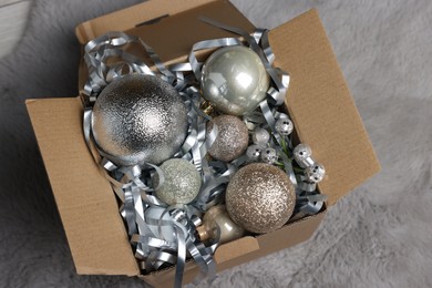 Photo of Shiny tinsel and Christmas balls in cardboard box on carpet, closeup