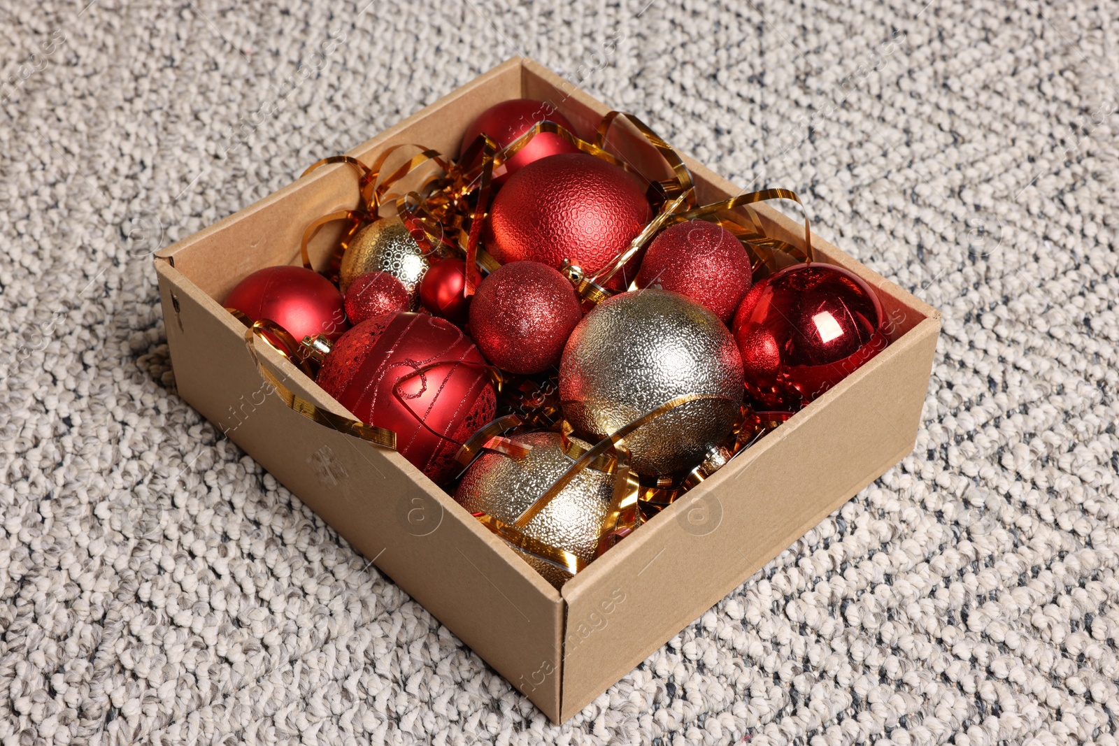 Photo of Shiny tinsel and Christmas balls in cardboard box on carpet