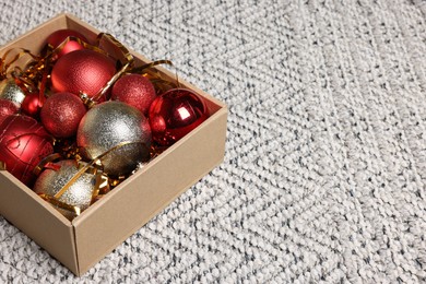 Photo of Shiny tinsel and Christmas balls in cardboard box on carpet, space for text