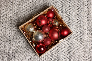 Photo of Shiny tinsel and Christmas balls in cardboard box on carpet, top view