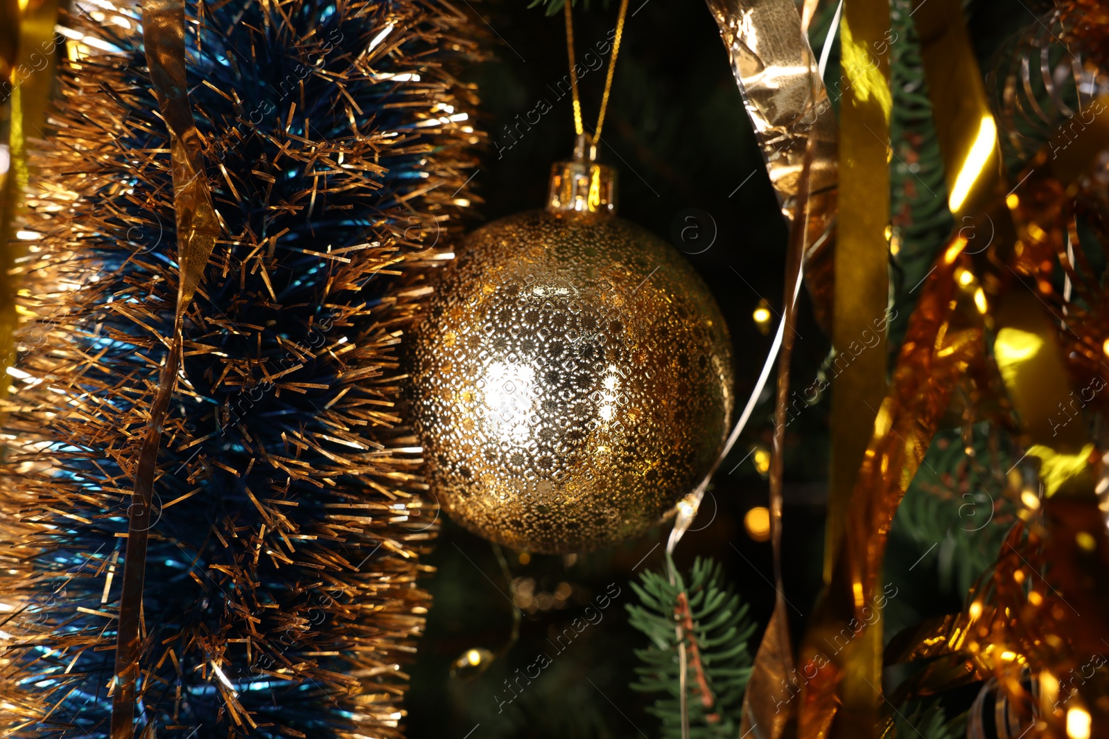 Photo of Shiny tinsel and golden ball on Christmas tree, closeup