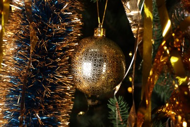 Photo of Shiny tinsel and golden ball on Christmas tree, closeup