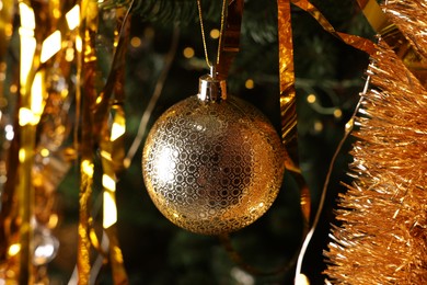 Photo of Shiny tinsel and golden ball on Christmas tree, closeup