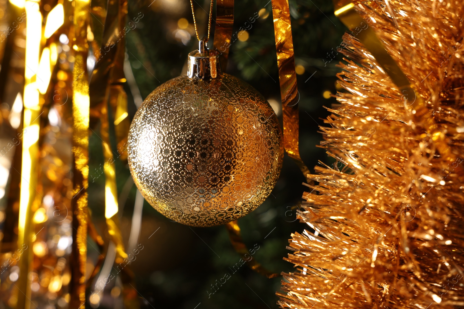 Photo of Shiny tinsel and golden ball on Christmas tree, closeup