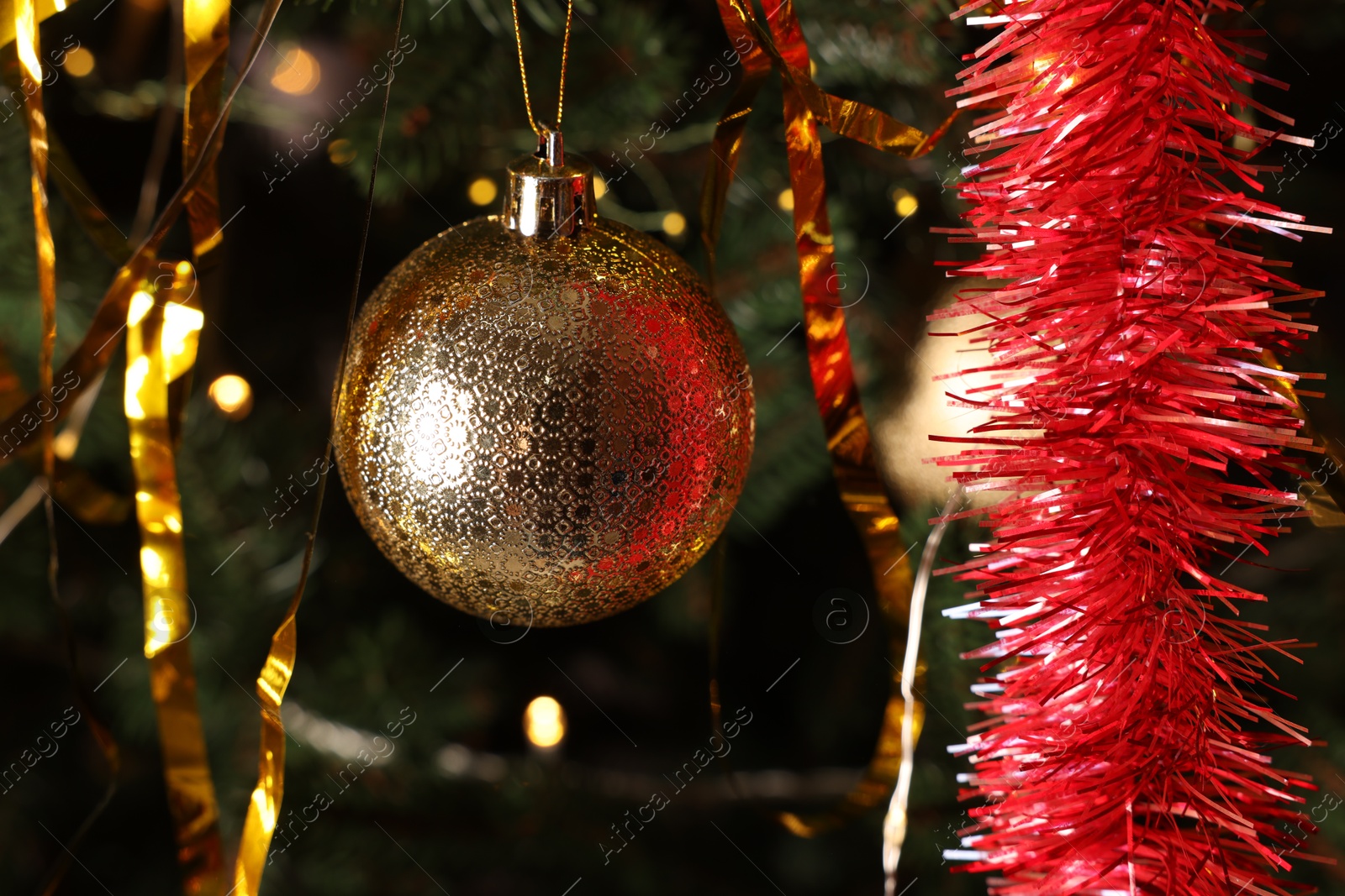 Photo of Shiny tinsel and golden ball on Christmas tree, closeup