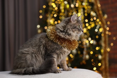 Photo of Cute cat with shiny Christmas tinsel on pouf indoors